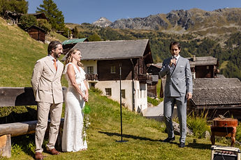 Charlotte and Derek standing before the officiant, the chalets in the background