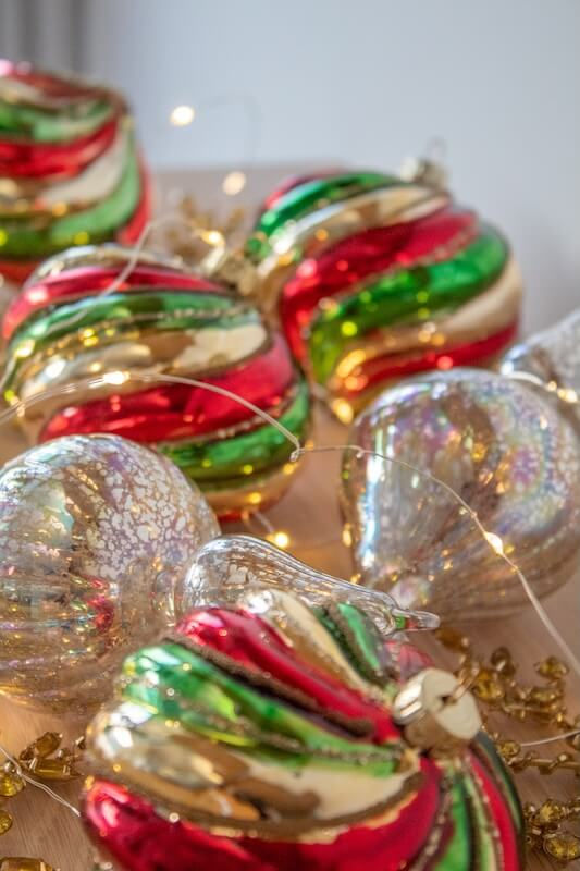 Festive red, green, and gold ornaments with string lights. Swirled patterns add sparkle. Warm, holiday ambiance in soft light setting.