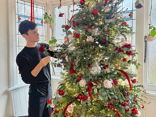 Professional Christmas tree decorator styling a Christmas tree with red ornaments, florals and greenery in a Sydney home.