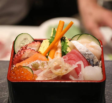 Assorted premium sashimi and seafood over sushi rice in a traditional chirashi box.