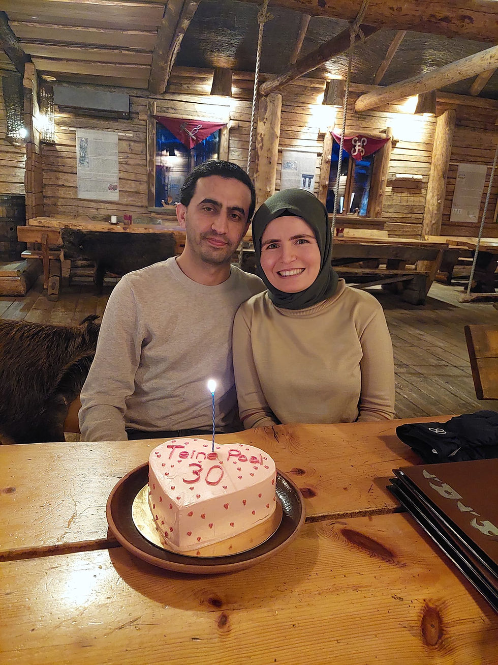 Smiling couple at a wooden table in a rustic restaurant, posing with a heart cake reading Teine Peal 30 and a lit candle.
