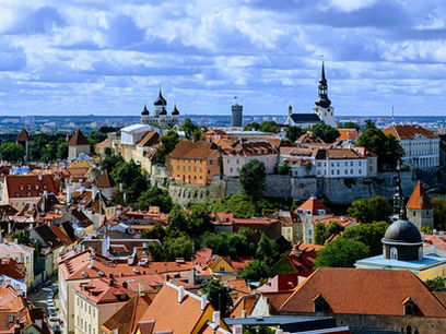 Panoramic view of Tallinn, Estonia, showing the historic Old Town with its red-tiled roofs, medieval towers, and church spires under a partly cloudy sky.