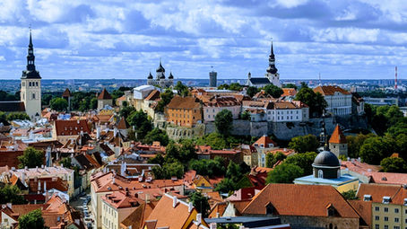 Panoramic view of Tallinn, Estonia, showing the historic Old Town with its red-tiled roofs, medieval towers, and church spires under a partly cloudy sky.