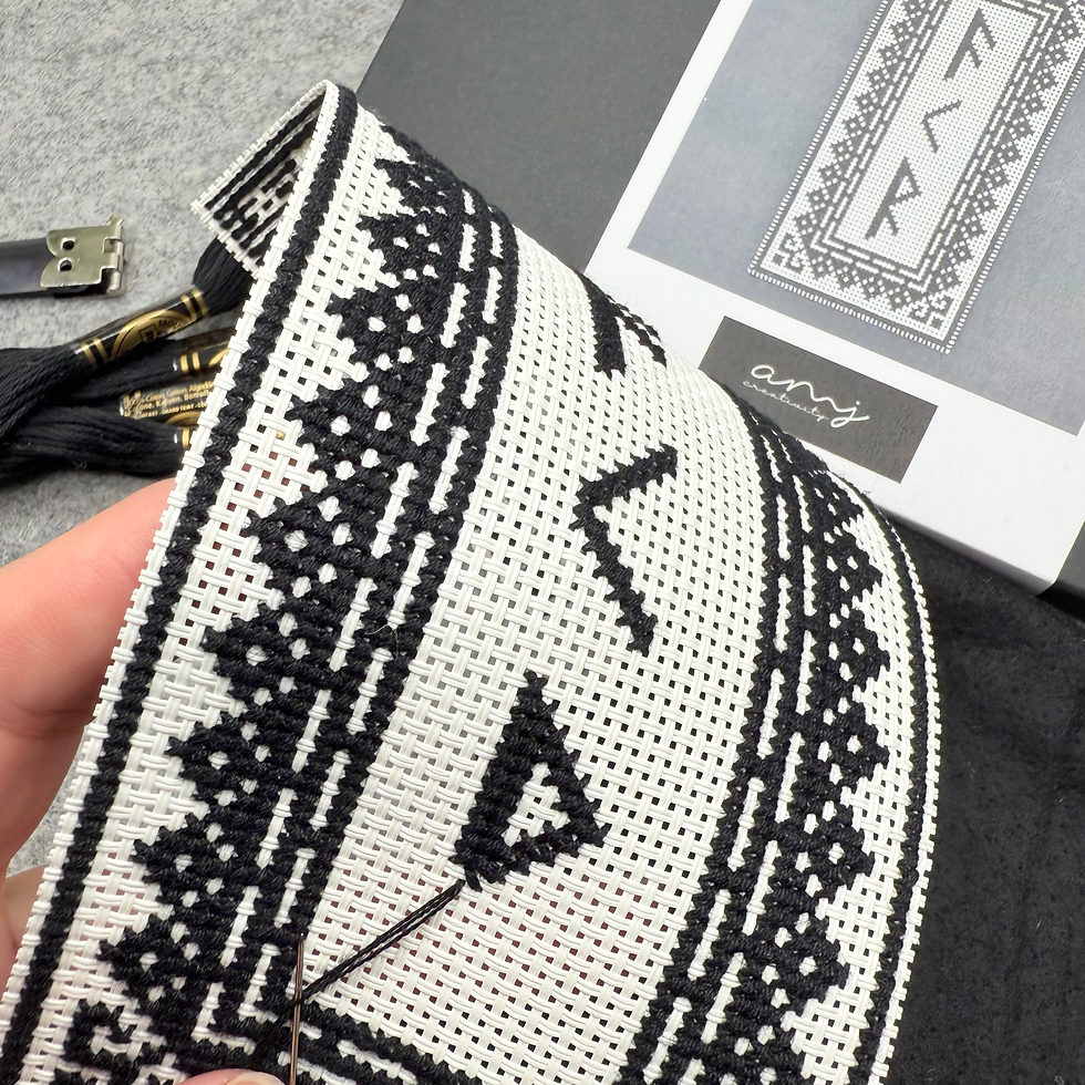 Hand stitching black geometric patterns on white fabric. A needle is in use. Background shows a printed design and black thread.