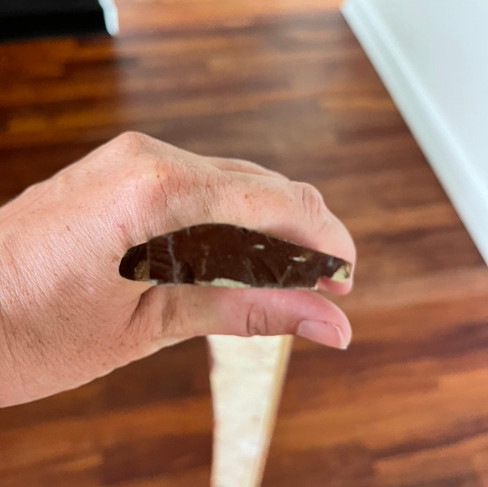 Hand holding a rubber door reducer that has been stained and blurry wood flooring in the background