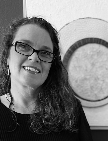 Anna Jonsdottir smiling with a picture of one of her art in the background, black and white picture