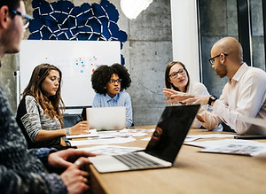 A group of five people sat around a table having a meeting