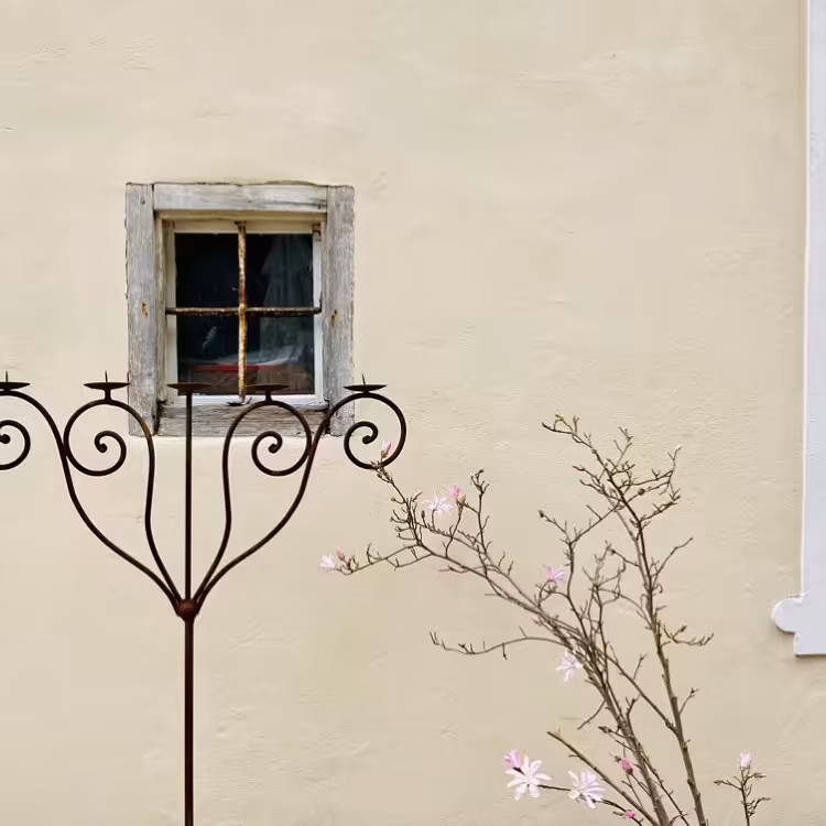 cremefarbene Fassade mit altem Fenster, Kerzenständer und Pflanze
