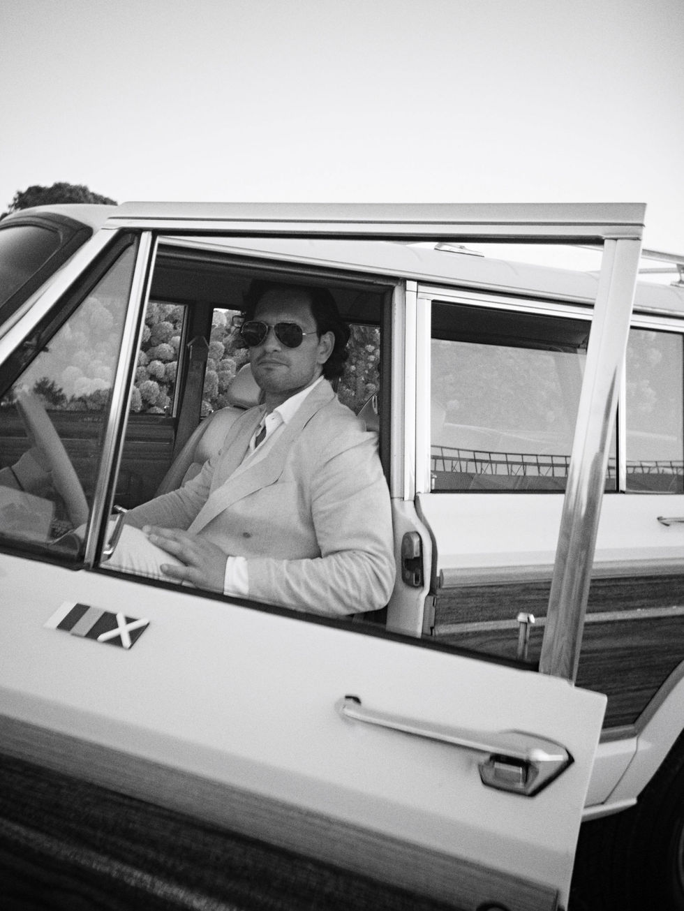 Man in suit sitting in vintage car, door open.