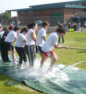 A team of young people taking part in a tug of war on a slip n' slide surface.