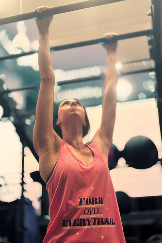 woman doing monkey bar hangs in a gym wearing a lfted fitness form over everything t shirt