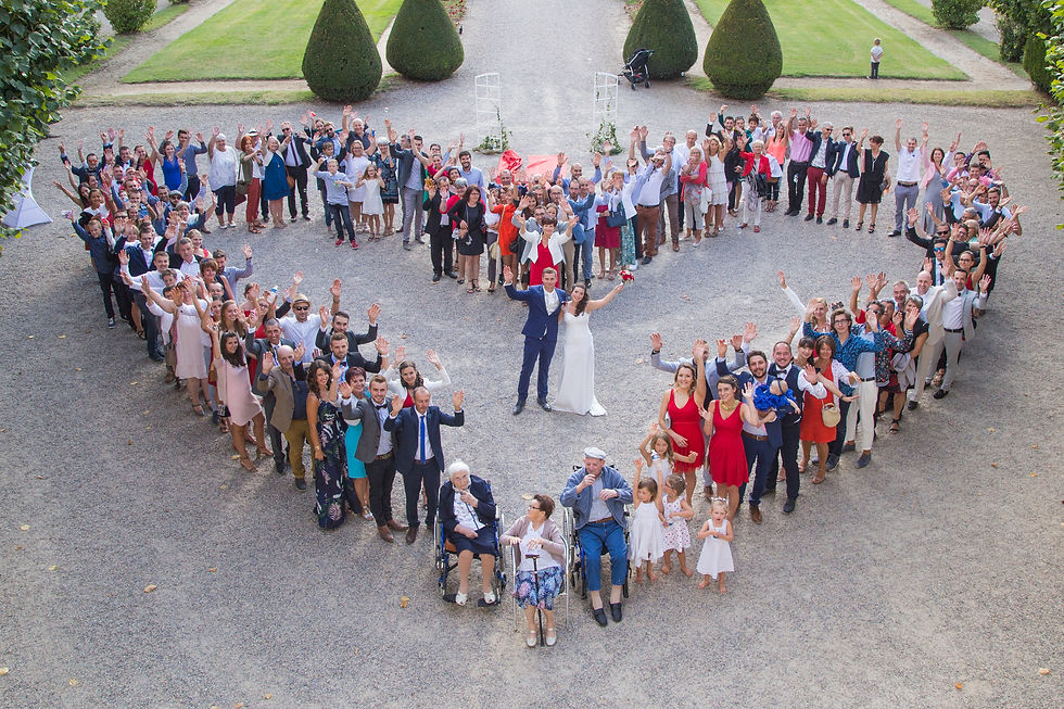 Groupe en forme de cœur avec un couple marié au centre. Les invités sourient et lèvent les bras. Jardin vert clair en arrière-plan.