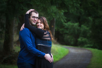 Couple souriant s'embrassant sur un sentier boisé et verdoyant.