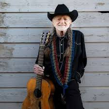 Willie Nelson against a white wall holding a guitar