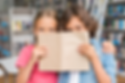 Zwei Kinder verstecken sich hinter einem braunen Buch in der Bibliothek.