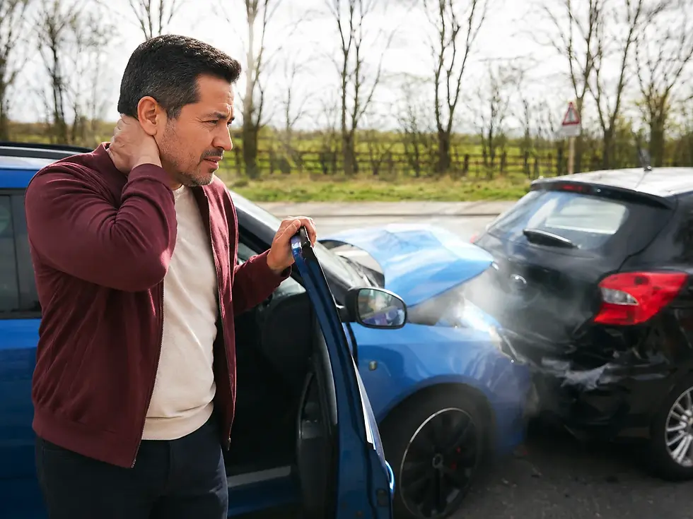 Man holding his neck in pain while standing beside two damaged cars after a collision.