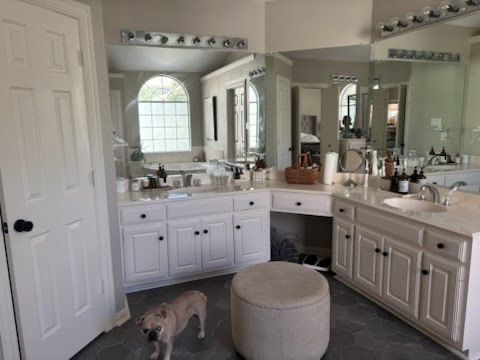 Old L-shaped white master bathroom vanity with theatrical strip lighting and sheet mirrors before luxury custom upgrade by a home remodeler in Dallas Fort Worth.