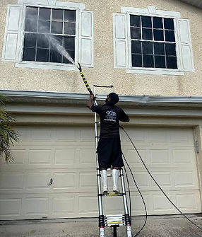 a man on a ladder pressure washes the house exteriors