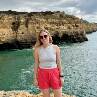 Woman wearing red shorts and sunglasses on a cliff over the ocean