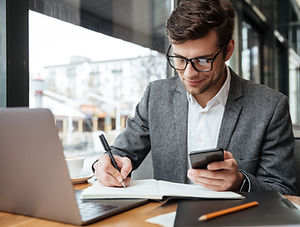 smiling-businessman-eyeglasses-sitting-by-table-cafe-with-laptop-computer-while-using-smar