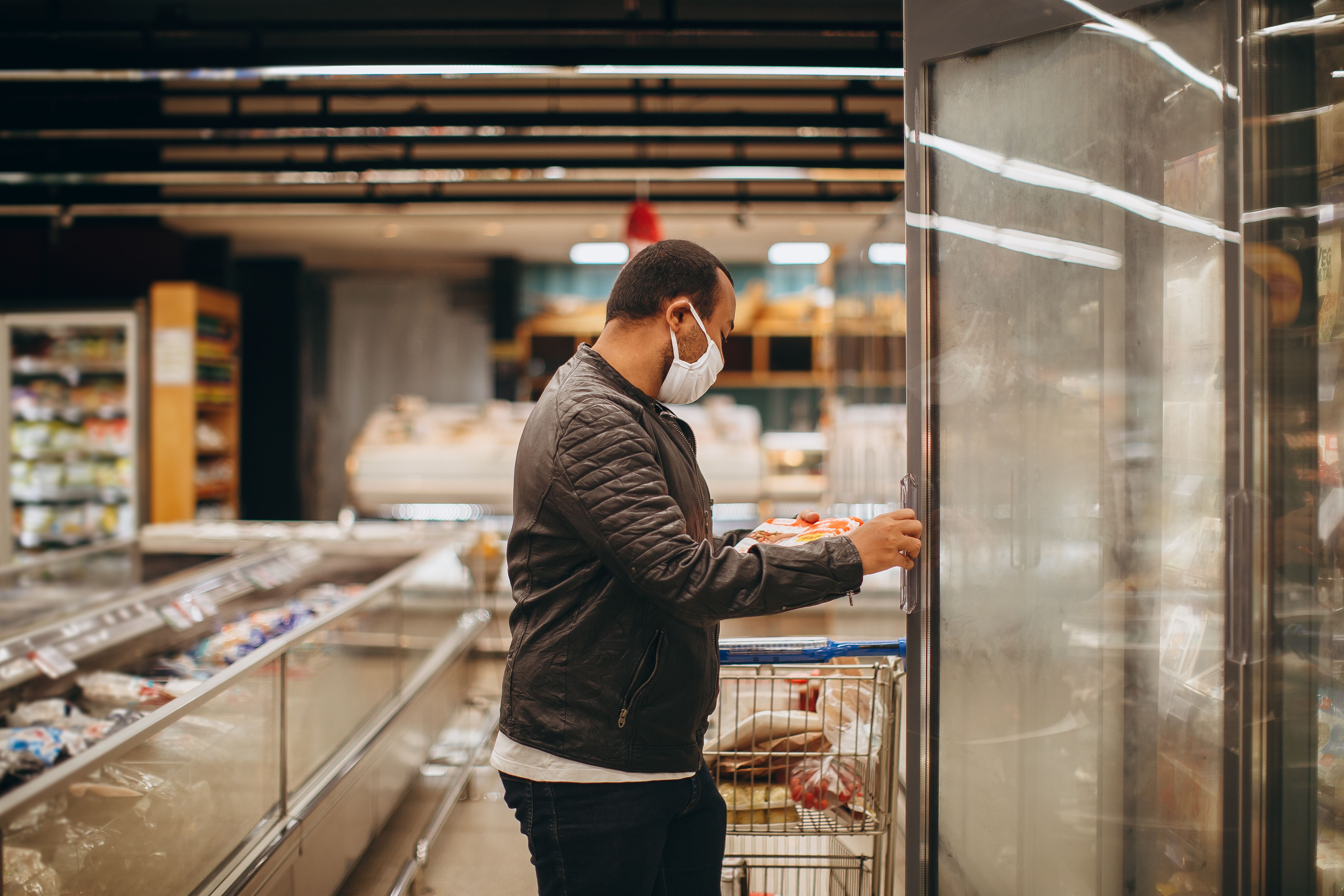 A shopper using an upright commercial freezer in a grocery aisle