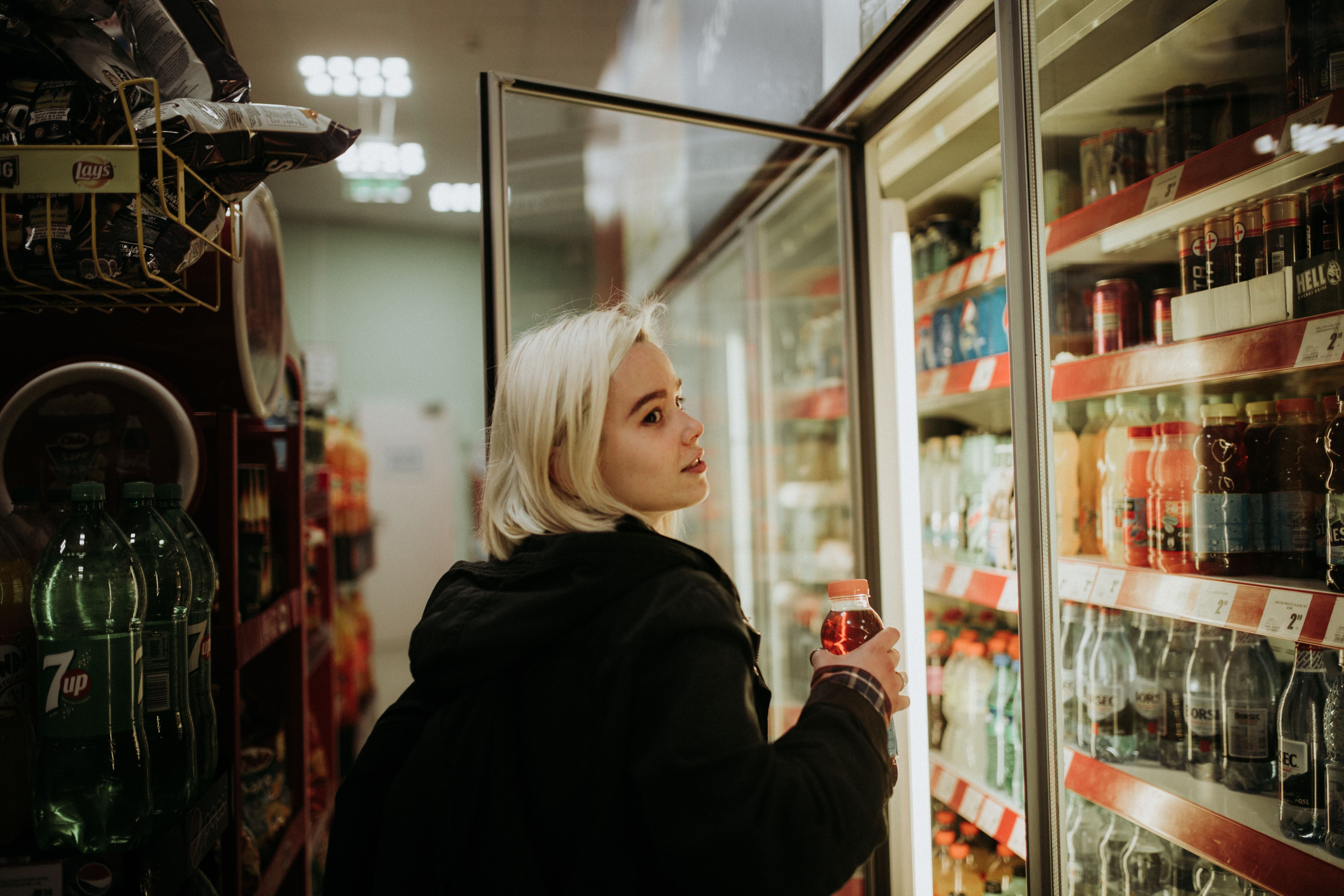 A customer selecting a drink from a glass-door store refrigerator