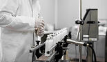 Worker in lab coat inspecting bottles on conveyor belt.