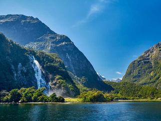 gorgeous lake in front of mountain with large cascading waterfall. Scene from New Zealand.