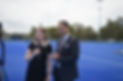 Two people being interviewed for television at a hockey field