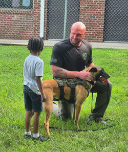K9 deputy kneels with his dog and talks to a student