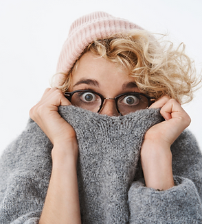 Photo of hip looking young woman with beanie and glasses pulling sweater over her face because she is afraid