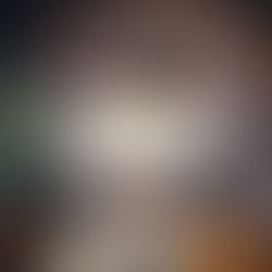 Person in hoodie lying on floor covered with various graphic hoodies, featuring "BARBARIC" text. Warm, relaxed atmosphere.