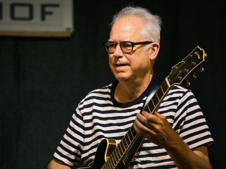 Gitarrist Bill Frisell mit Brille und gestreiftem Shirt spielt E-Gitarre auf einer Bühne