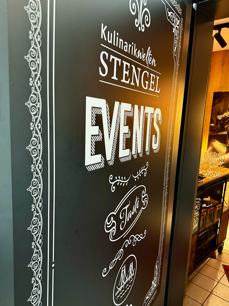 Schild für Events der Kulinarwelten Stengel mit eleganter weißer Schrift und Verzierungen auf dunklem Hintergrund, betonend auf kulinarische Verkostungen.