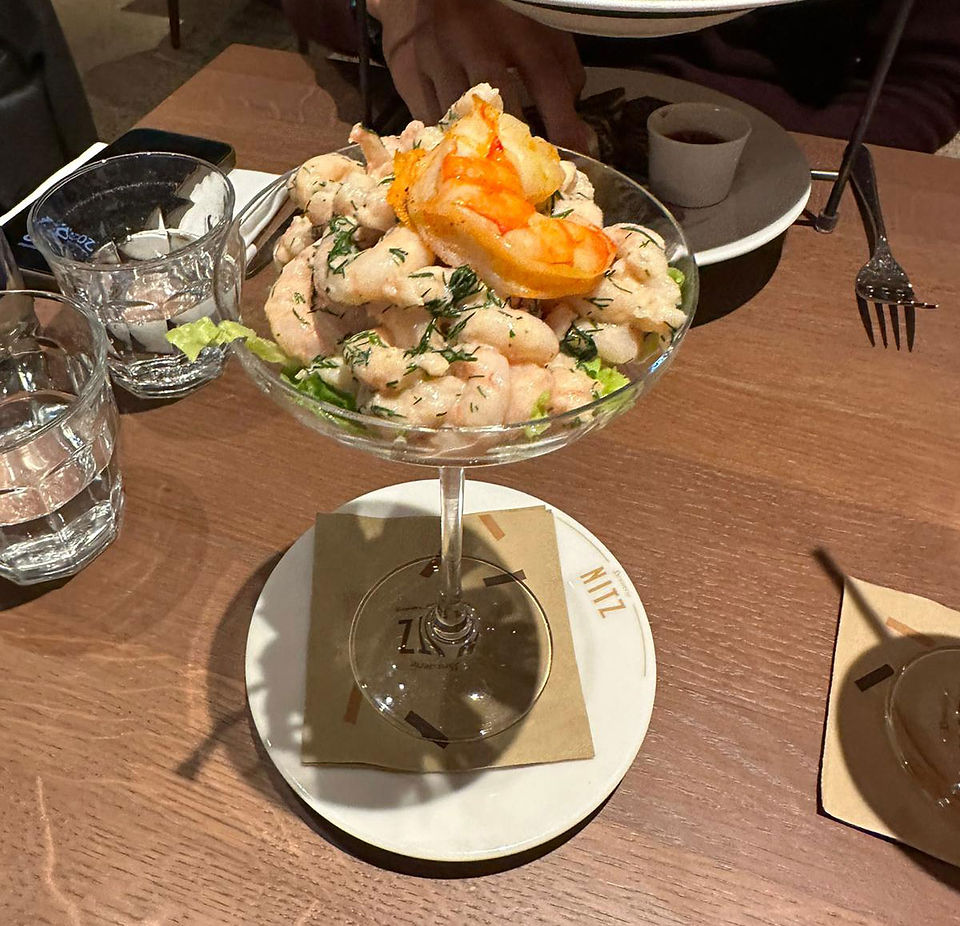 Ein Krabbencocktail, serviert in einem Glasschälchen, gekrönt mit einer großen Garnele und mit Dill garniert, präsentiert in der Brasserie Nitz.