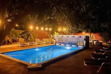 Sfeervol verlicht zwembad in de avond bij Bonaire Fun & Tropicana, omringd door ligbedden en tropisch groen.