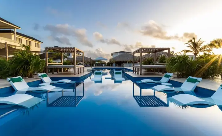 Stijlvol resort op Bonaire met luxe loungebedden in het zwembad en tropische sfeer bij zonsondergang