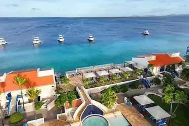 Luchtfoto van het Divi Flamingo Beach Resort op Bonaire met oranje daken, zwembad en zonnebedjes, uitkijkend over de helderblauwe Caribische zee waar enkele boten voor anker liggen