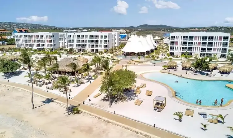 Modern strandresort op Bonaire met witte gebouwen, tropische palmbomen en lagunezwembad aan zee