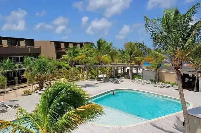 Toegankelijk resort op Bonaire met zwembad, palmbomen en ligbedden onder een strakblauwe lucht