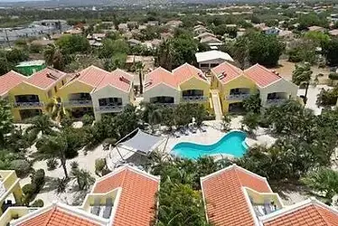 Luchtfoto van Bonaire Village, met kleurrijke appartementen rondom een tropisch zwembad, omgeven door palmbomen en groene tuinen