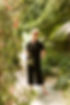 Friendly massage therapist standing in a lush tropical garden walkway, radiating calm and confidence — promoting natural wellness and personalized therapeutic care.