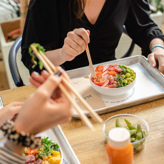 en una mesa hay dos comensales que disfrutan de su poke bowl sentados en una mesa de madera con luz natural