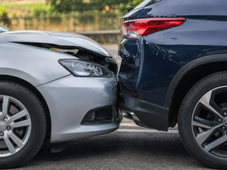 Silver car’s crumpled front bumper presses into the rear of a dark blue SUV in a roadside collision scene.