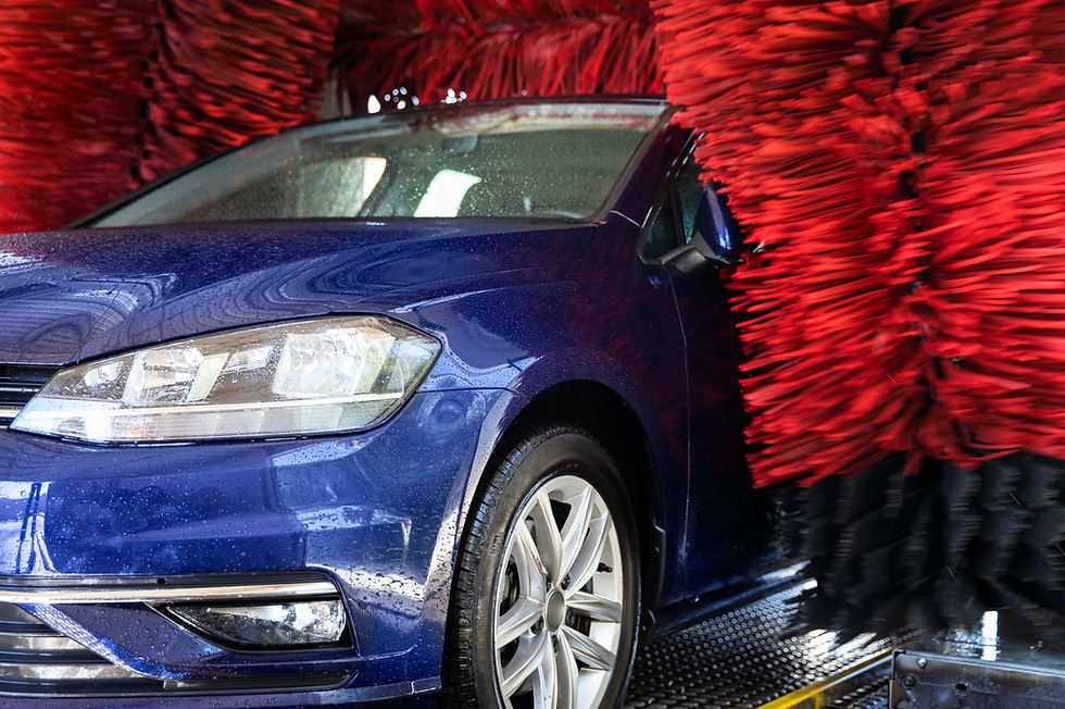Blue sedan in a car wash as red spinning brushes scrub the side and front, wet and glossy.