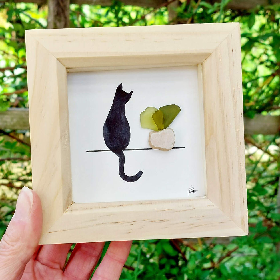 Thumbnail: A hand holding a picture of a watercolour black cat next to a plant made from watercolour and sea glass.