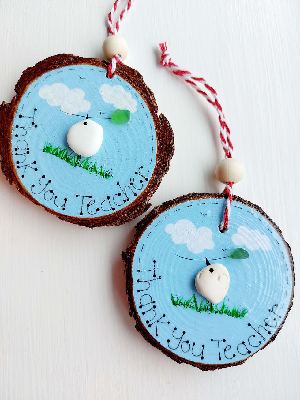Thumbnail: Two blue painted wood slices decorated with the hand written words, 'Thank you Teacher' and a pebble bird