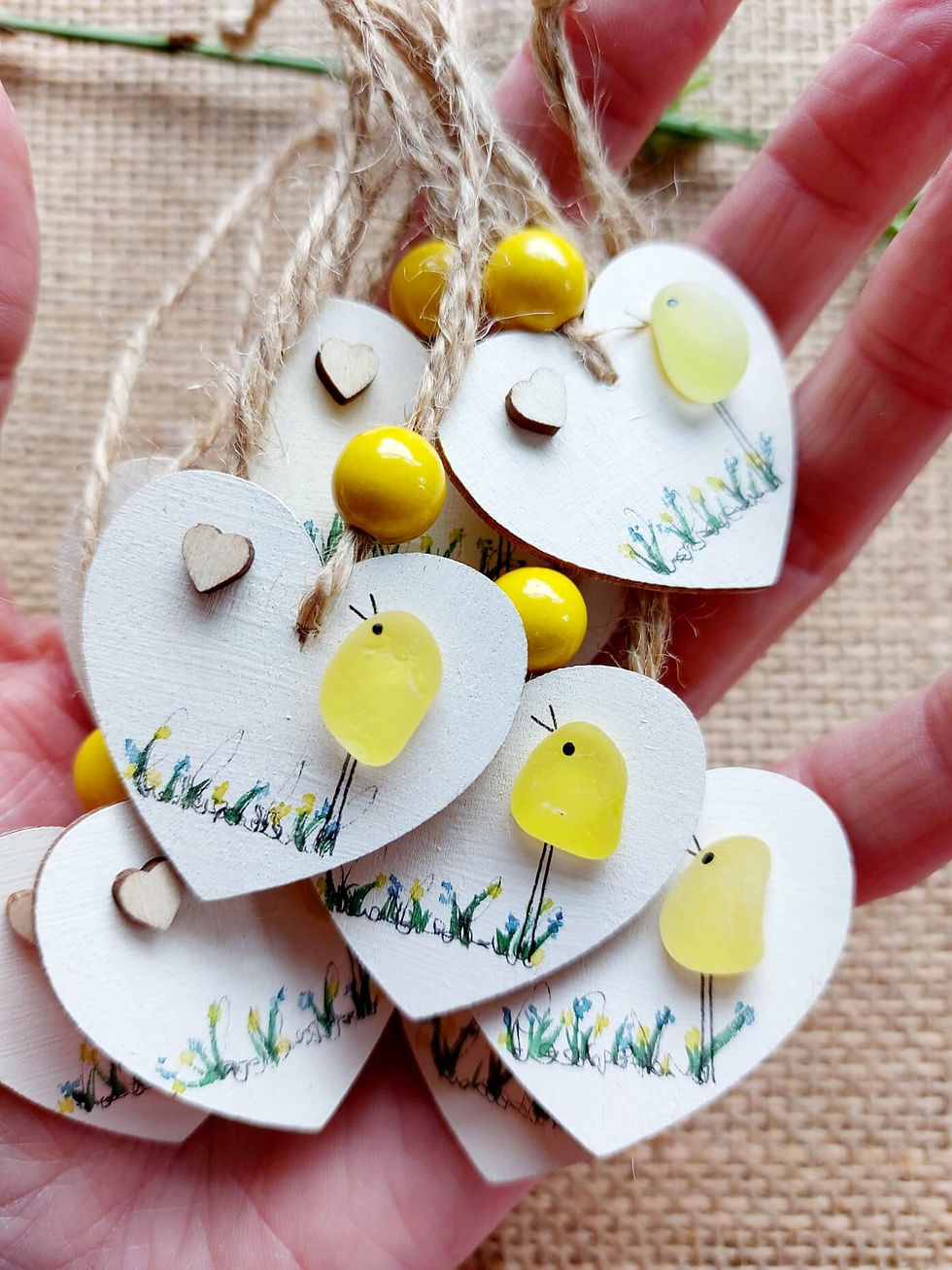 Thumbnail: Hand holding white hand painted hearts decorated with a yellow sea glass bird, watercolour details and a tiny wooden heart.