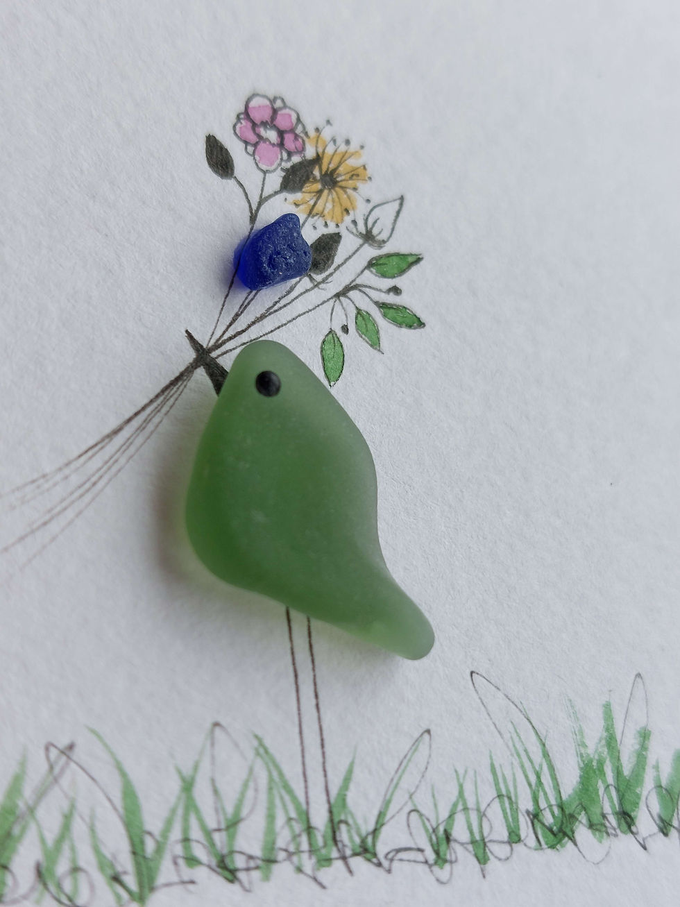 Thumbnail: Close up of a picture of a bird holding flowers in its beak. The bird is made from sea glass and the flowers are hand painted