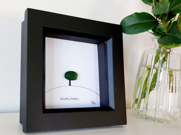 A black framed picture of a tree on a hill made with a single piece of green sea glass.